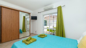 A bedroom with a bed, green towels, a TV, and a window with curtains.