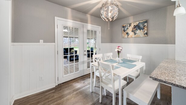 A dining area with a white table and chairs, a decorative ceiling light, and a view through glass doors to an outdoor seating area. - 4 bedroom house near, 15 min from Magnolia (Waco)