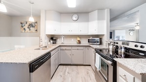 A modern kitchen with white cabinets, a stainless steel dishwasher, a microwave, and a stove. - 4 bedroom house near, 15 min from Magnolia (Waco)