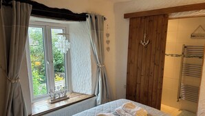 A bedroom with a bed, a window with curtains, a wooden door, and a towel rack. - A beautiful family holiday cottage with lots of character in an idyllic village (Ulverston)