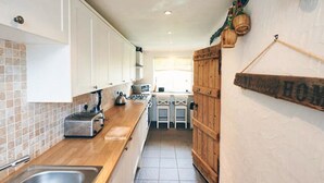 A narrow kitchen with white cabinets, a wooden countertop, and a tiled backsplash. - A beautiful family holiday cottage with lots of character in an idyllic village (Ulverston)