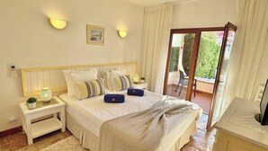 Un dormitorio con cama, mesitas de noche, televisor y balcón con vistas al verdor.