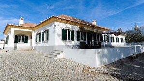 Ein weißes Gebäude mit grünen Fensterläden und einem Ziegeldach, mit einem Kopfsteinpflasterhof.