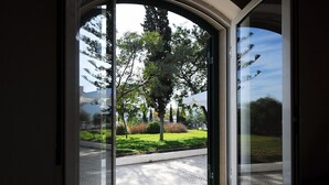 Ein Fenster mit Blick auf eine gepflasterte Fläche, Bäume und ein ferner Berg.