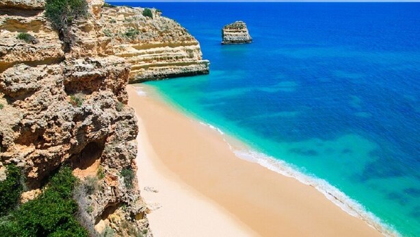 Un paisaje costero con una playa arenosa, acantilados rocosos y un mar azul cristalino.