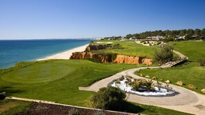 Campo de golf con vista a la playa, un camino sinuoso y una zona ajardinada con rocas y plantas.