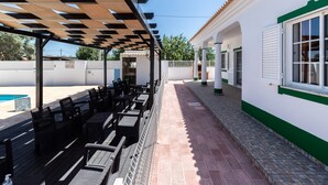 Un patio al aire libre con mesas y sillas de madera, piscina y un paseo cubierto.