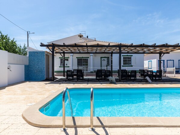 A swimming pool with a pergola and lounge chairs in a sunny outdoor area.