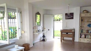 A spacious room with a large window, a small table, a wooden bench, and a bookshelf. - Beautiful villa with sea view, large garden and private access to the beach (Marbella)
