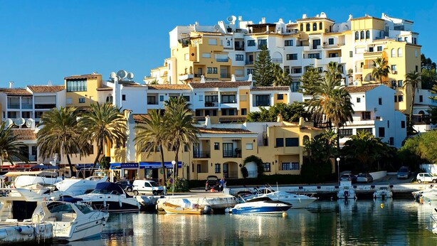 A marina with boats docked, a building with balconies, and palm trees. - Beautiful villa with sea view, large garden and private access to the beach (Marbella)