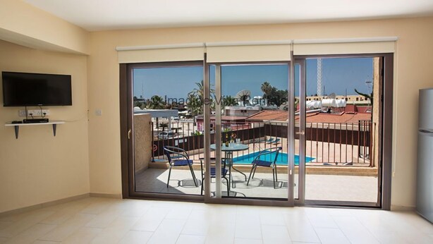 Amplia sala de estar con un gran ventanal corredero que da a un balcón con piscina y mobiliario exterior.