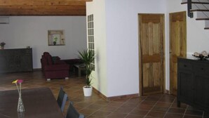 Een ruime woonkamer met een houten plafond, een eettafel met stoelen, een bank en een potplant.