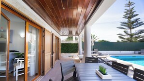 Een overdekt terras met zwembad, houten plafond en buitenmeubilair.