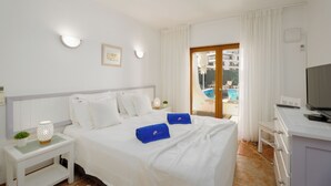 Een hotelkamer met een bed, een bureau, een televisietoestel en uitzicht op een zwembad.