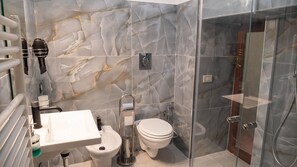 Une salle de bain moderne avec un pare-baignoire en marbre, une douche en verre, des toilettes et un lavabo avec un robinet.