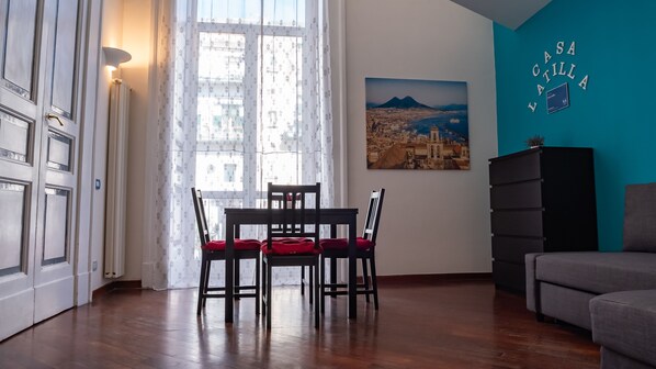 Un salon comprenant une table à manger, des chaises, un canapé, un téléviseur fixé au mur et une fenêtre avec des rideaux.