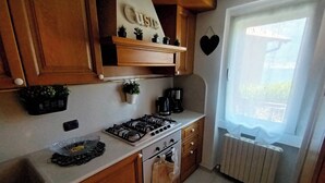 Une cuisine avec des meubles en bois, une cuisinière à gaz, une machine à café et une fenêtre donnant sur un paysage verdoyant.