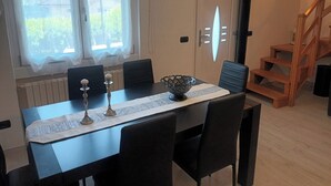Un coin repas avec une table dressée pour quatre personnes, deux chaises de chaque côté, un bol décoratif et des bougeoirs. Un escalier est visible sur la droite, menant à un niveau supérieur.
