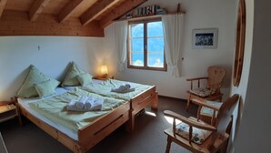 A cozy room with a wooden bed, a small wooden chair, a nightstand with a lamp, and a window with curtains.