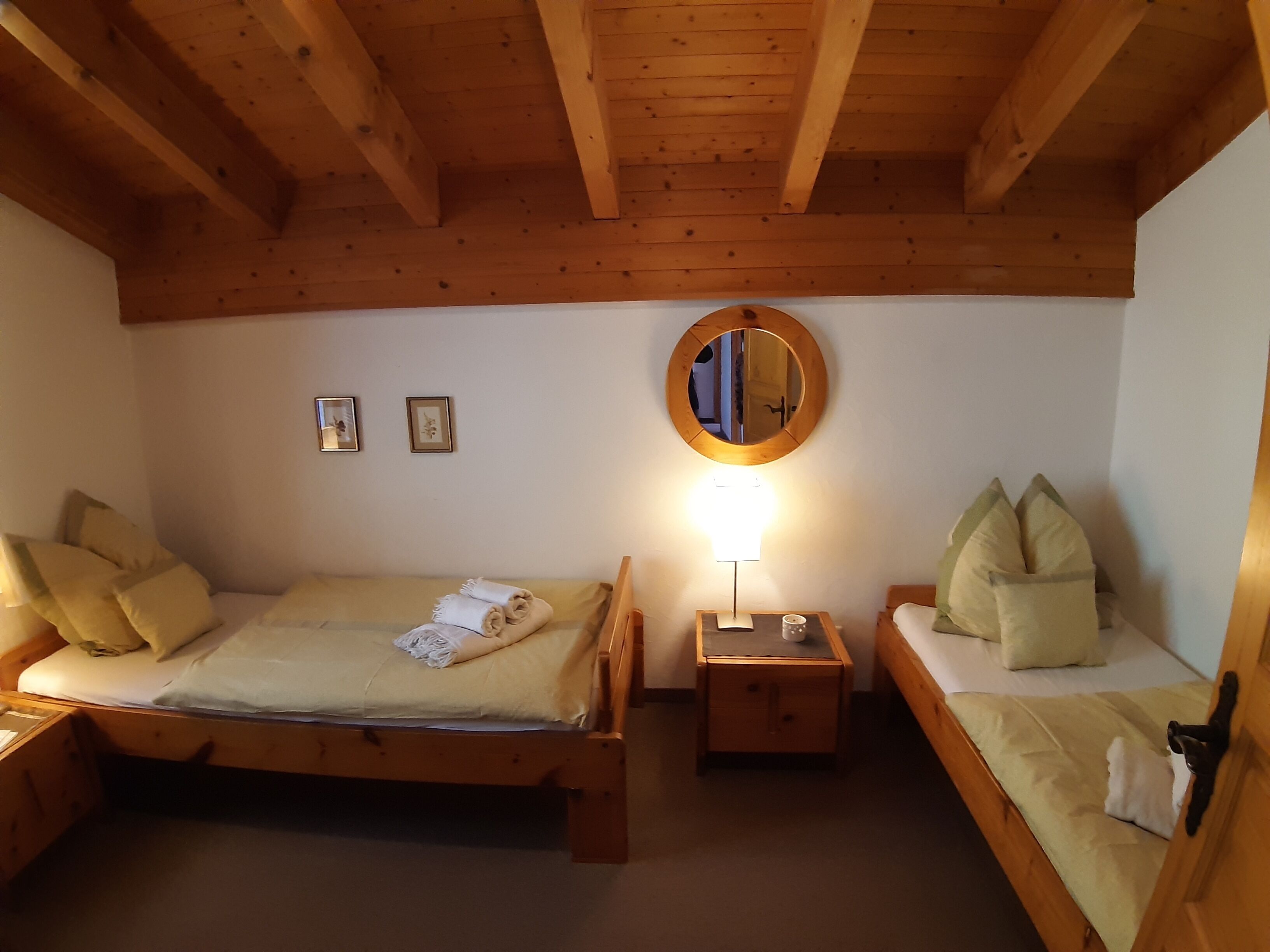 A wooden room with two beds, a nightstand, a mirror, and framed pictures on the wall.