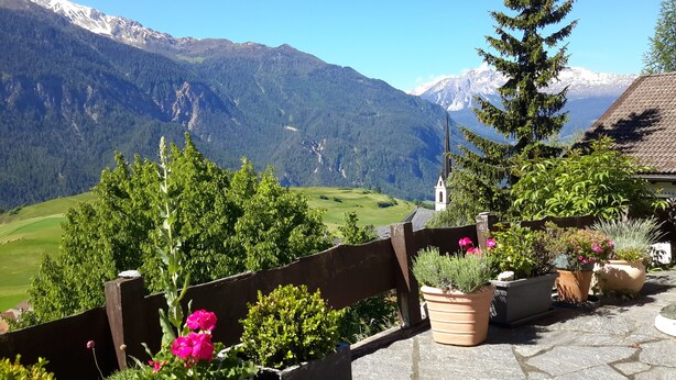 A scenic view of a mountain landscape with a church and a wooden fence with potted plants.