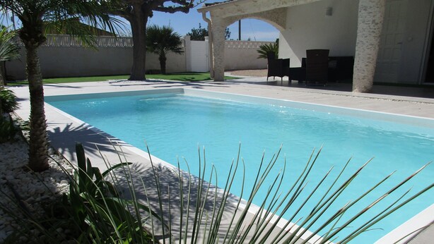 A swimming pool with a clear blue water, surrounded by a white wall and a covered patio area with chairs. - “Ampolla Villa”, 5 min away from the beach, 500 sqm garden, 9 persons (L' AMPOLLA)