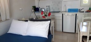 Ett kompakt hotellrum med en säng, ett litet skrivbord, ett litet kök och ett badrum.