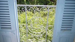 En hvid metalport med detaljeret ornamentering, der fører til en frodig grøn have.