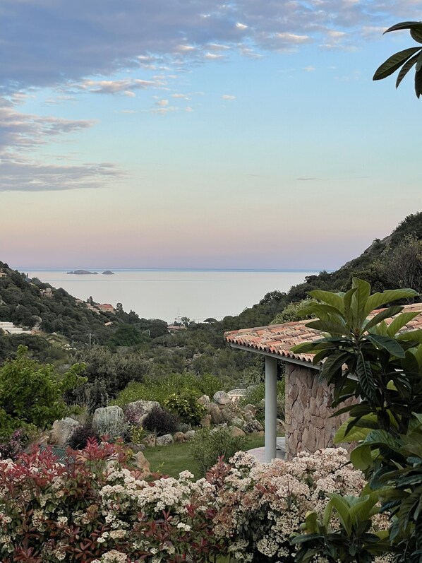 A coastal landscape with a stone structure, lush greenery, and a view of the sea.