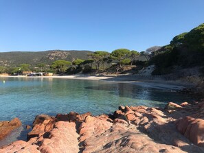 Paesaggio costiero con acque limpide, costa rocciosa e un edificio sullo sfondo con una spiaggia.
