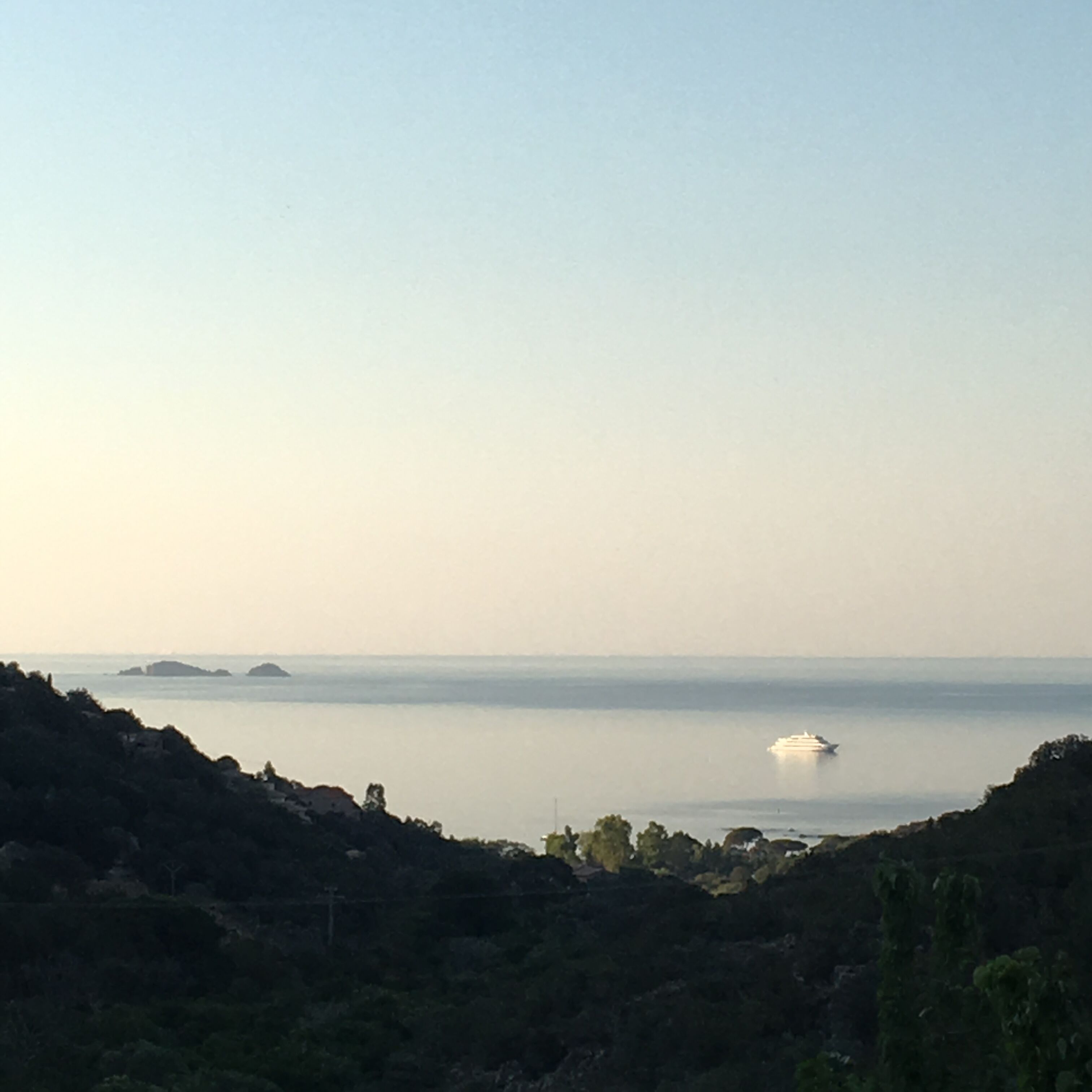 A coastal landscape with a clear view of the sea, distant islands, and a boat.