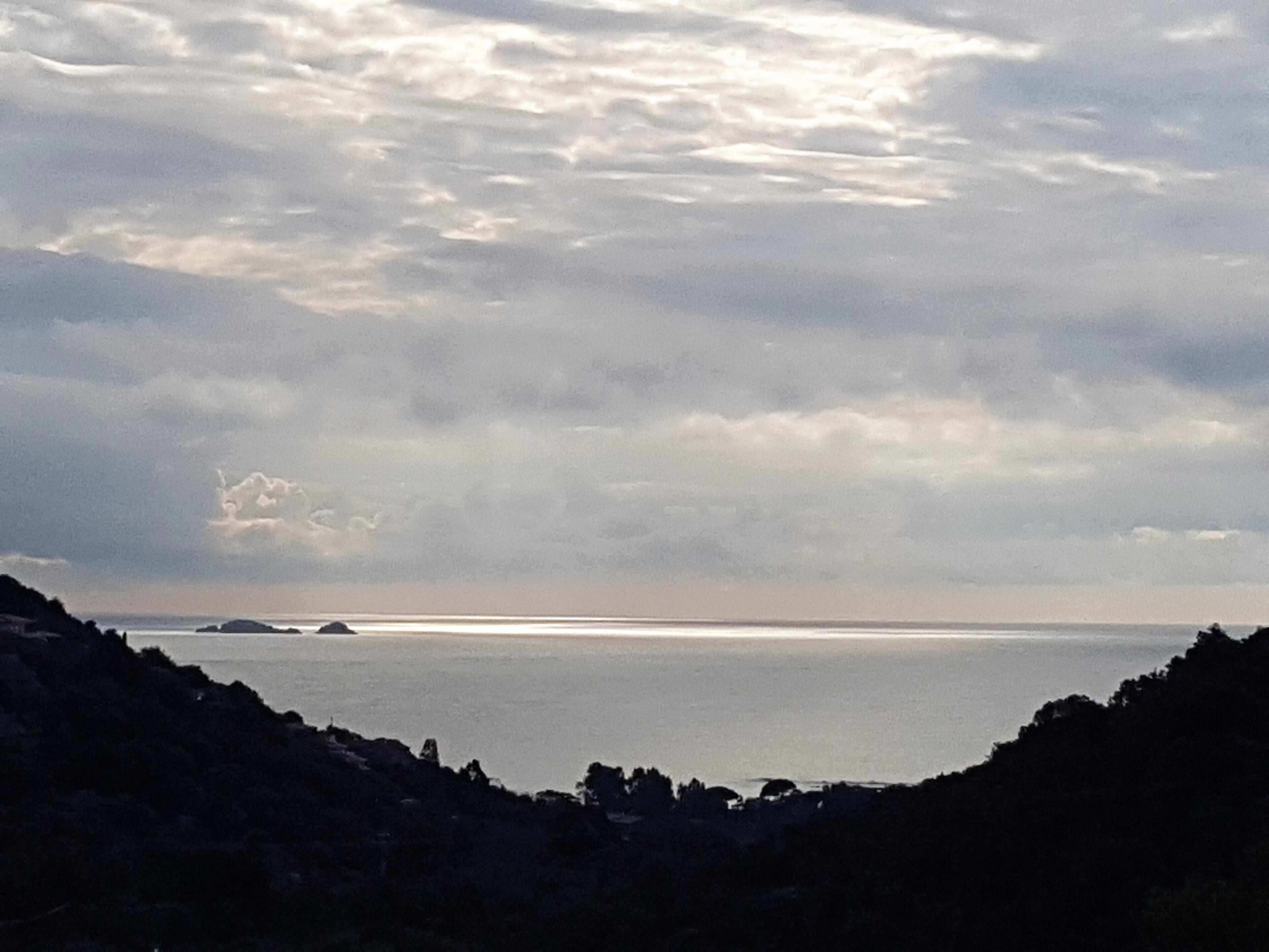 Paisaje costero con vista al mar y a islas distantes bajo un cielo nublado.