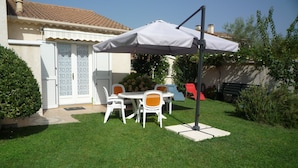 A patio with a table and chairs under a white umbrella, a red chair, and a white door with patterned glass. - apartment F1,1 room, 1 kitchen, 1 bathroom possibility 4 pers. (Vescovato)
