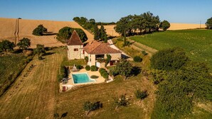 Una casa de piedra con una torre, rodeada de campos y árboles.