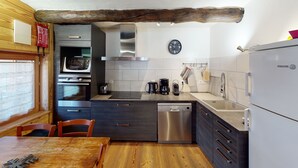 Et kompakt køkken med moderne hårde hvidevarer, trædetaljer og et rustikt loft.