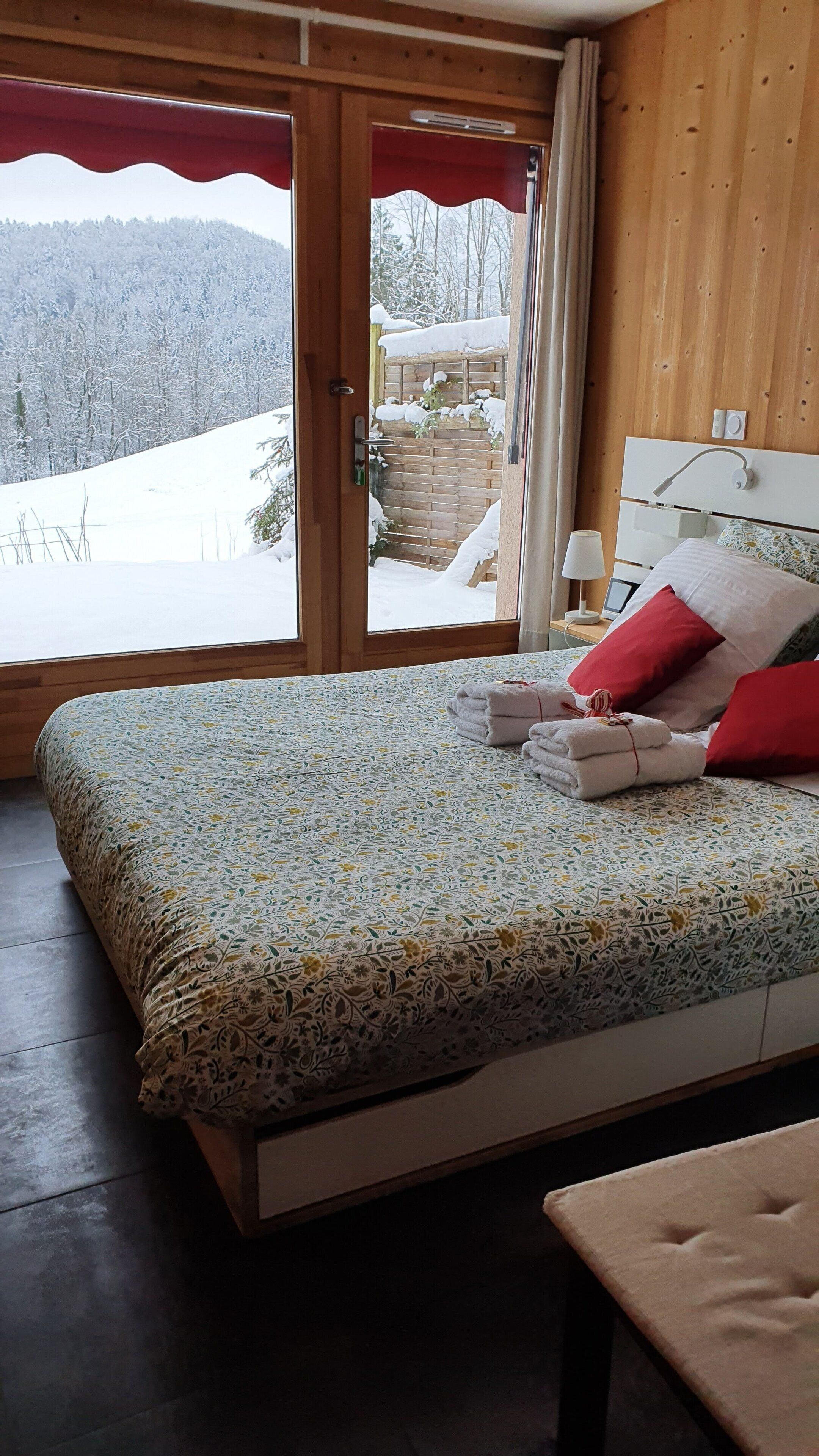 Un dormitorio con cama, almohadas y vistas a un paisaje nevado a través de una puerta de cristal.