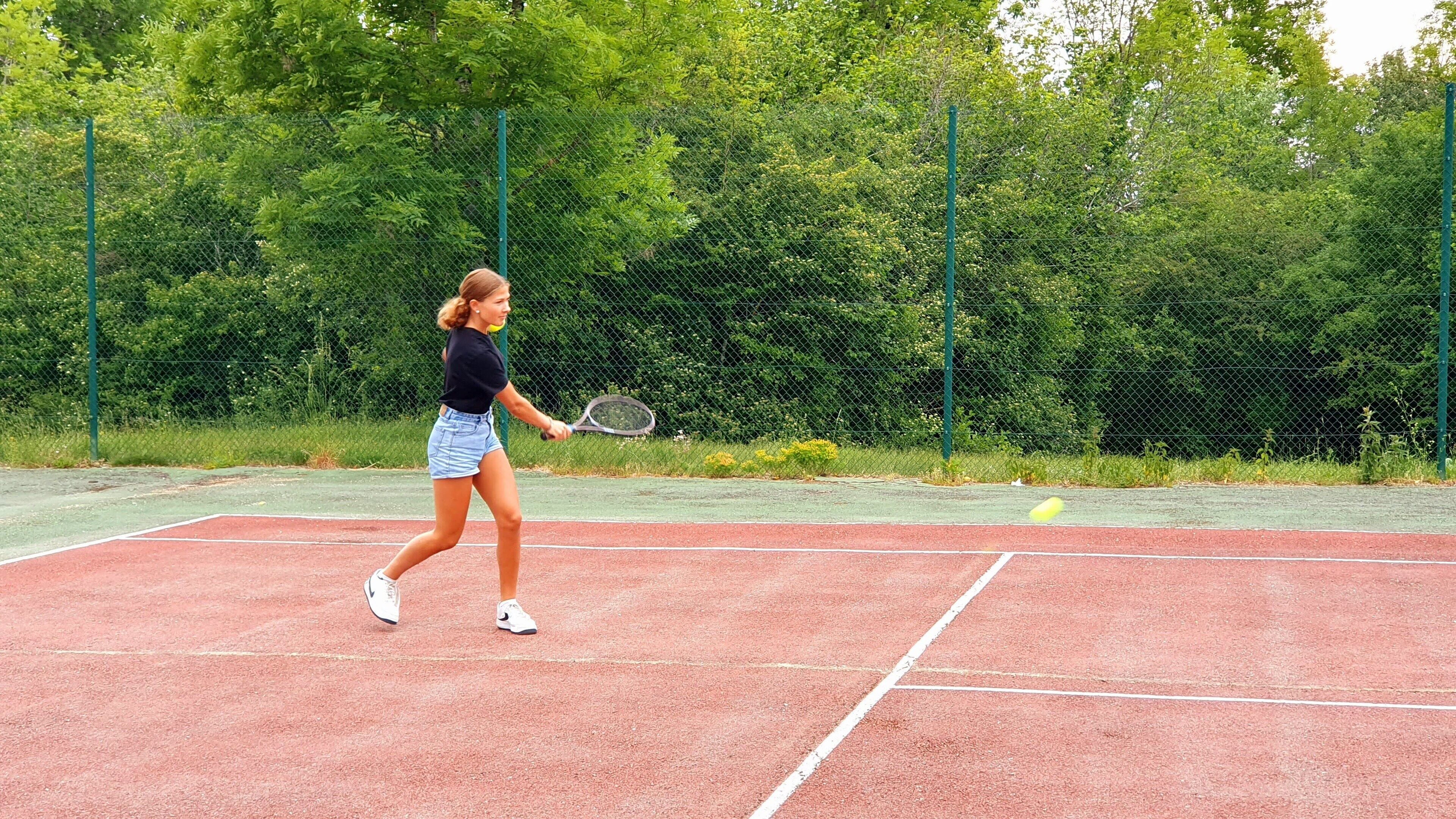 Una cancha de tenis con una red, rodeada por una cerca de malla y árboles.