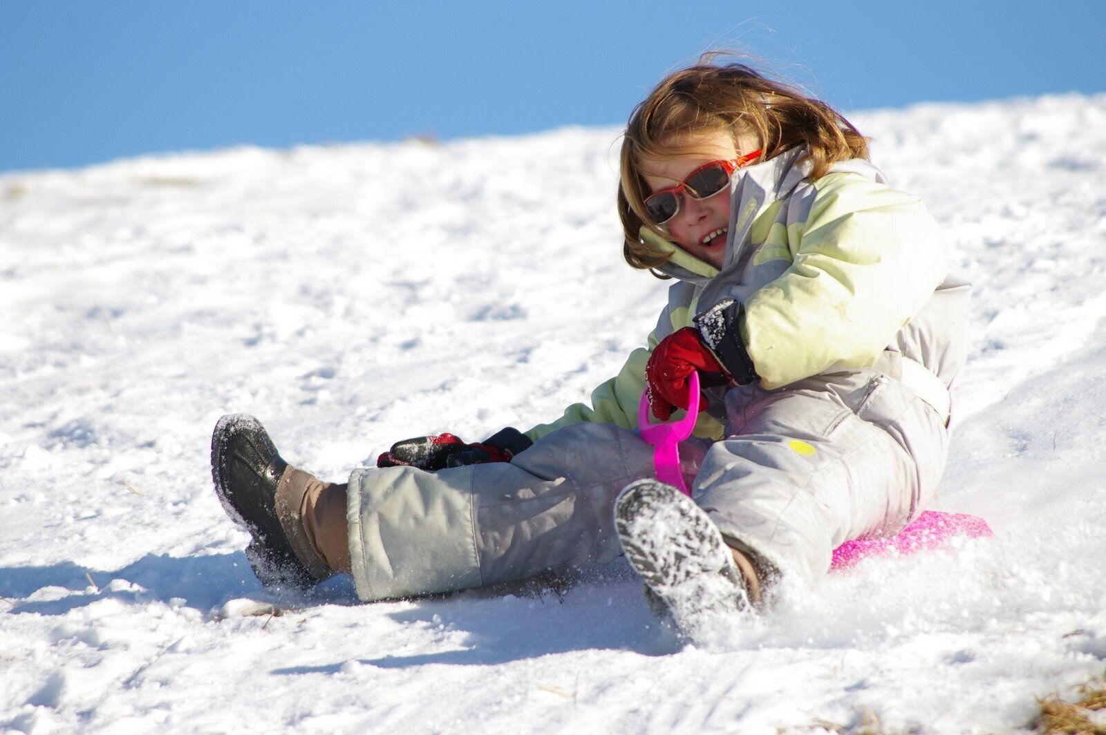 Une personne assise sur la neige, portant une veste et des gants.