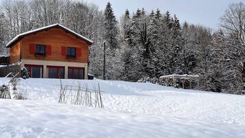 Una cabaña de madera con contraventanas rojas y un techo cubierto de nieve, rodeada de árboles cargados de nieve.