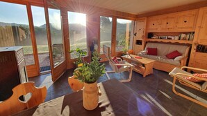 A cozy living room with wooden furniture, large windows, and a view of the outdoors.