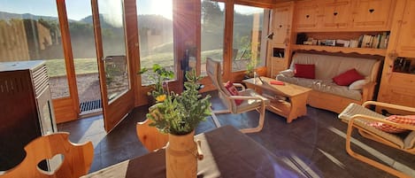 En hyggelig stue med møbler af træ, store vinduer og udsigt til naturen.