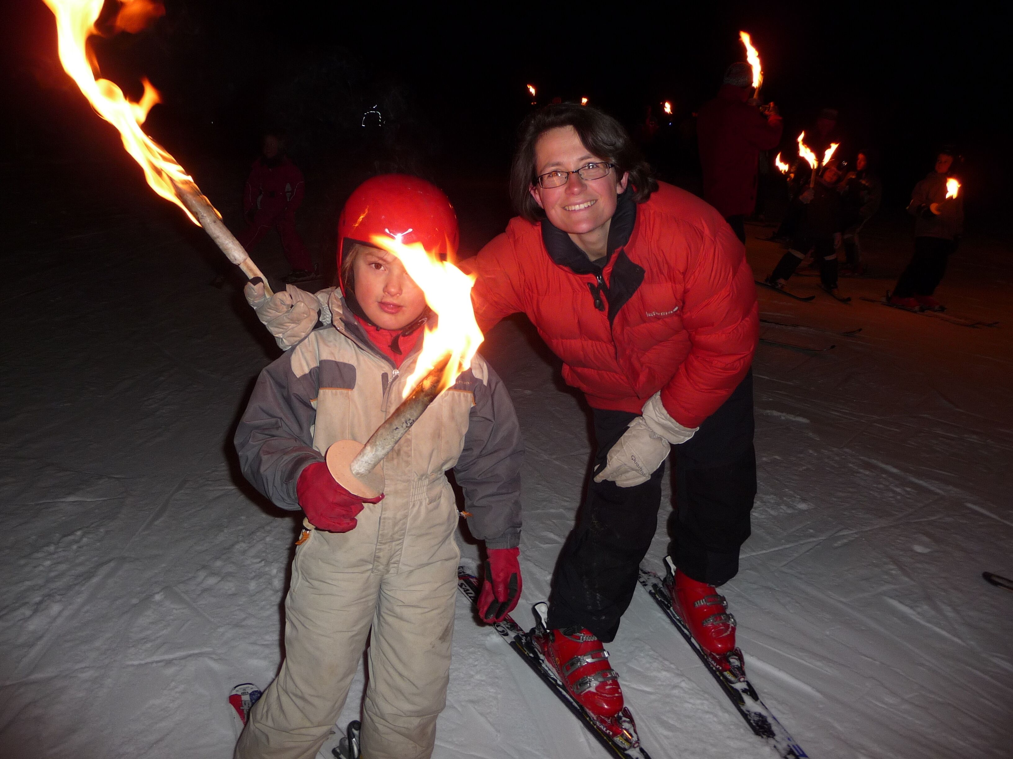 A person holding a torch, another person in a red jacket, and a snowy environment.