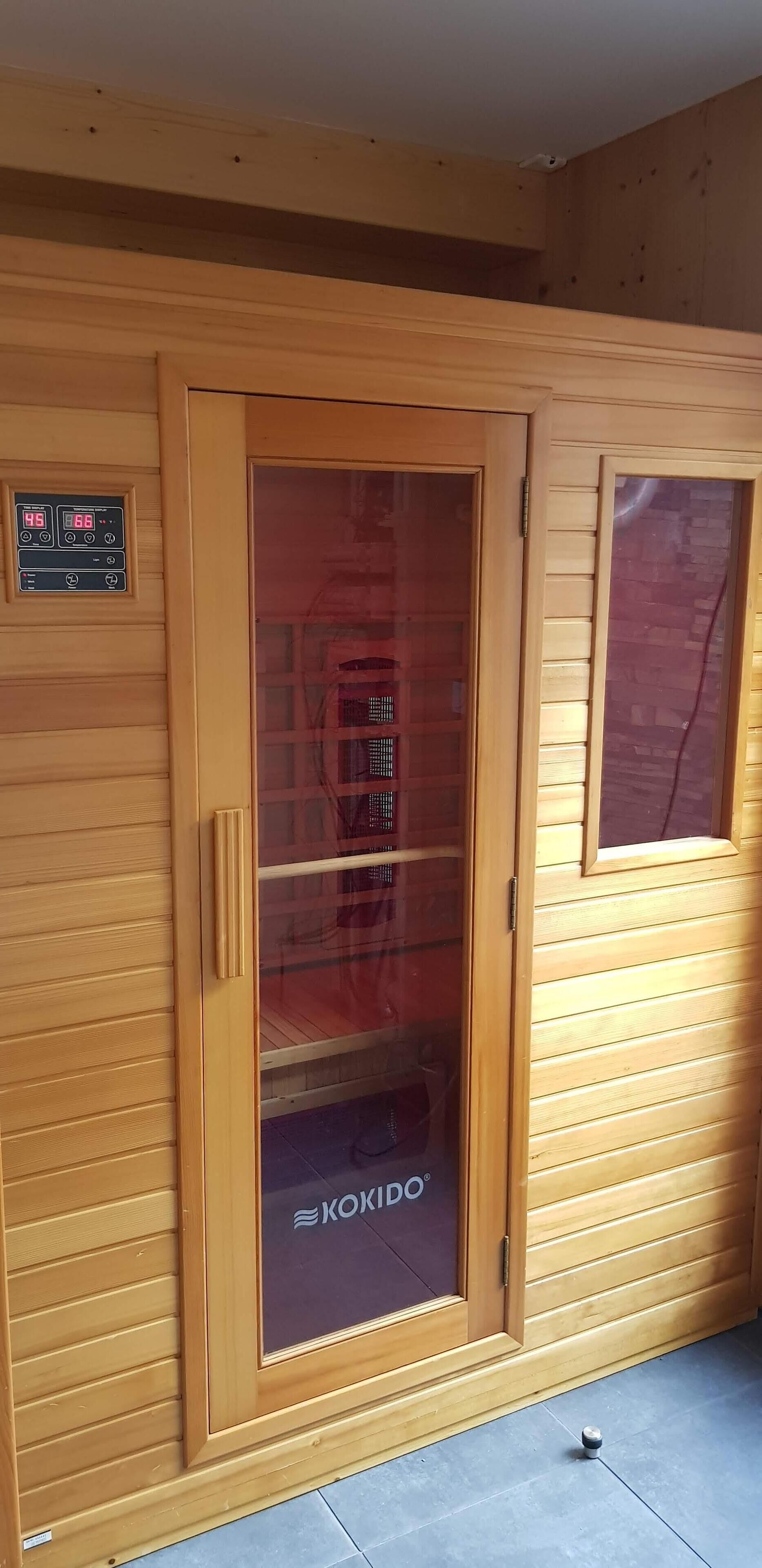 Een houten deur met een ruit en een bedieningspaneel aan de muur.