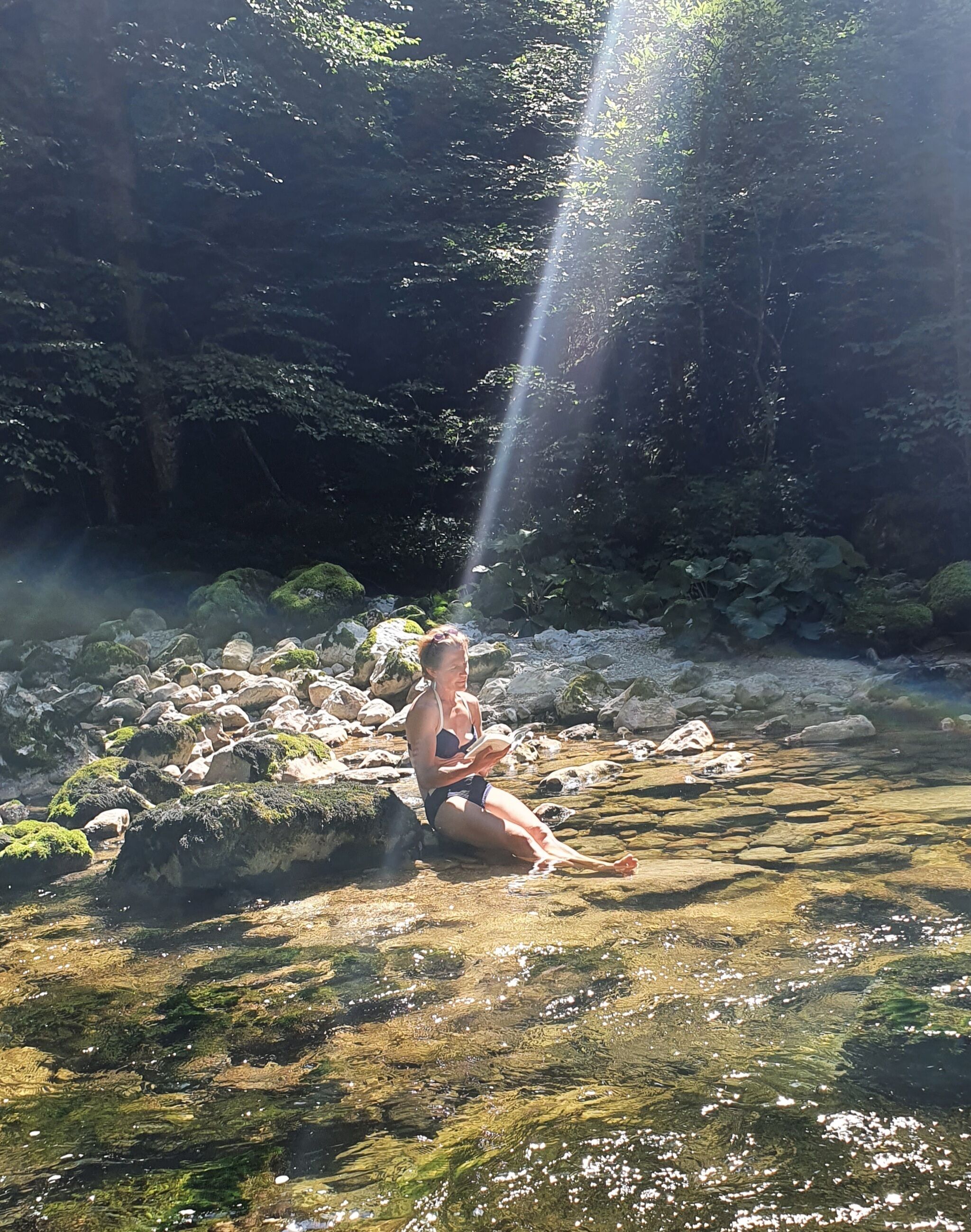 A person sitting on rocks by a clear stream in a natural setting.
