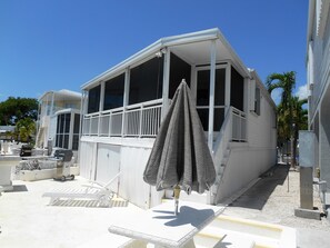 Un bâtiment blanc doté de grandes fenêtres et d’un balcon, avec des meubles d’extérieur et un espace abrité.