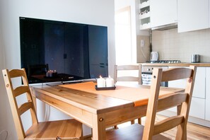 A dining area with a wooden table and chairs, a flat-screen TV, and a kitchen in the background.
