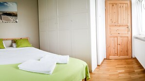 A bedroom with a bed, green bedding, a white towel, a wooden door, and a window. - Sopot Sleeps - Sopot Suite (Sopot)