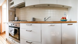 A modern kitchen with white cabinets, a wooden countertop, a gas stove, a sink, and a bowl of fruit. - Sopot Sleeps - Sopot Suite (Sopot)