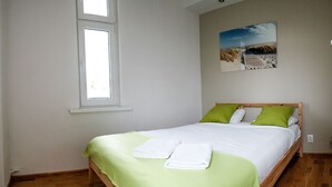 A neatly made bed with green and white bedding, a wooden headboard, and a window with blinds. - Sopot Sleeps - Sopot Suite (Sopot)