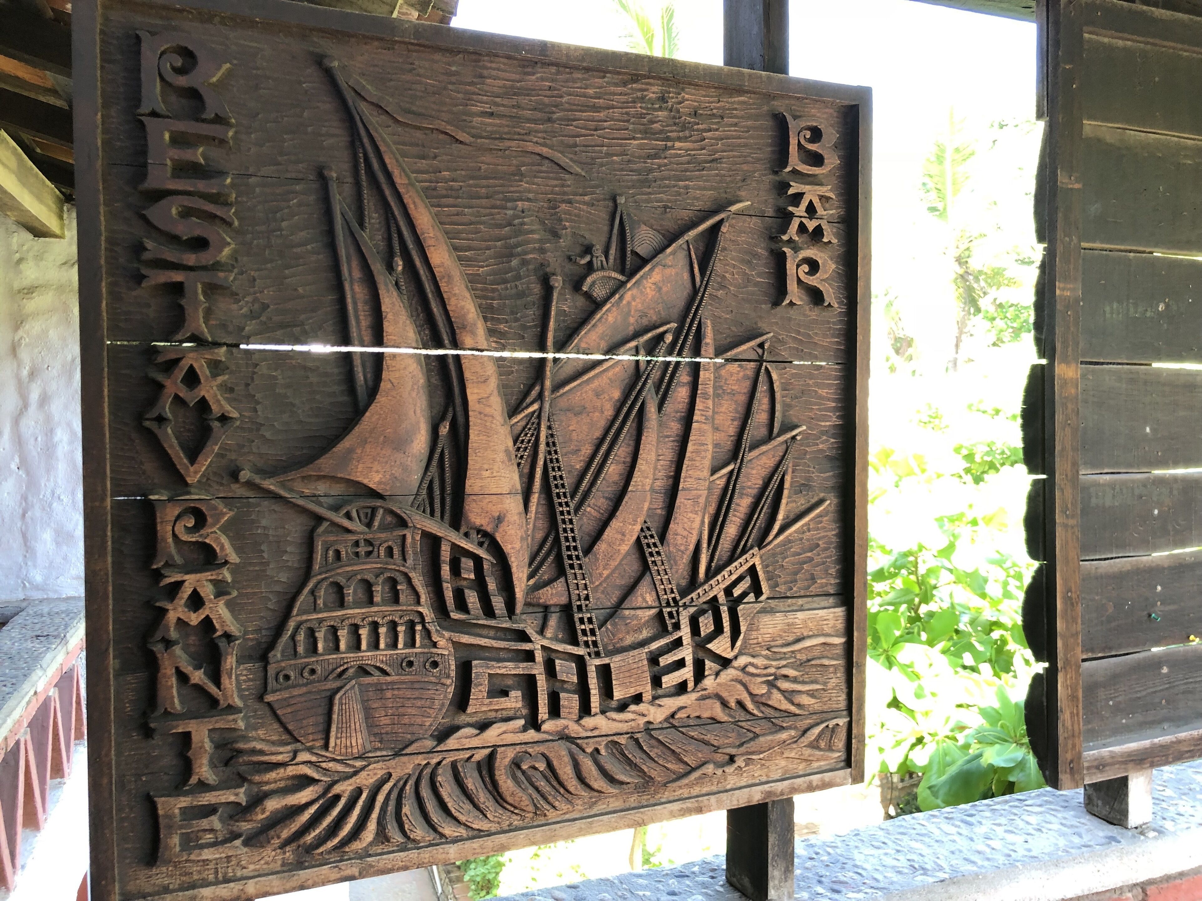 Ein hölzernes Schild mit eingravierten Schiffen und Wellen, das ein Hafenmotto andeutet.